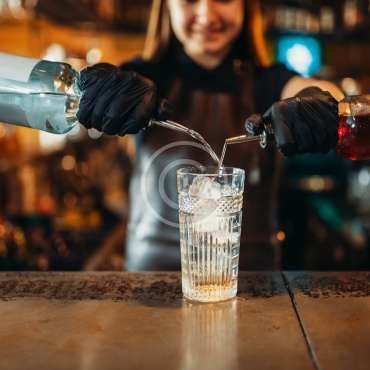 Woman bartender mixing alcoholic coctail. Alcohol drink preparation. Female barman working at the bar counter in pub